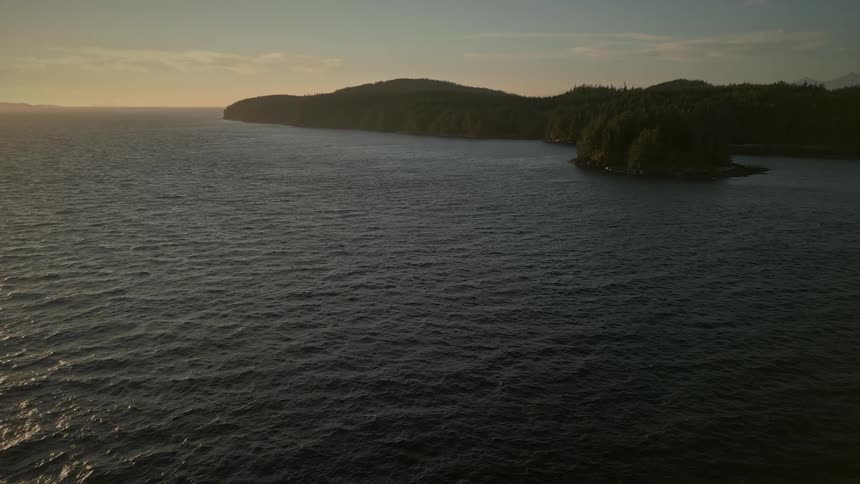 An aerial of a small island next to a forested coastline at sunset