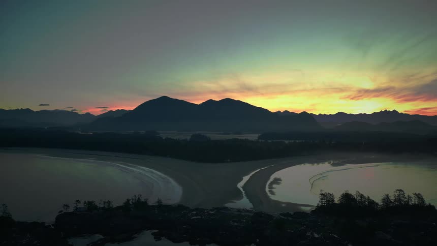 Aerial view of a beach with mountains on the horizon and the reddish sunrise