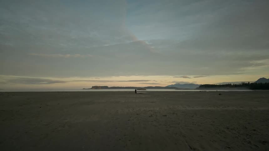 Person stands silhouetted on sand under red tinted sky on foggy morning