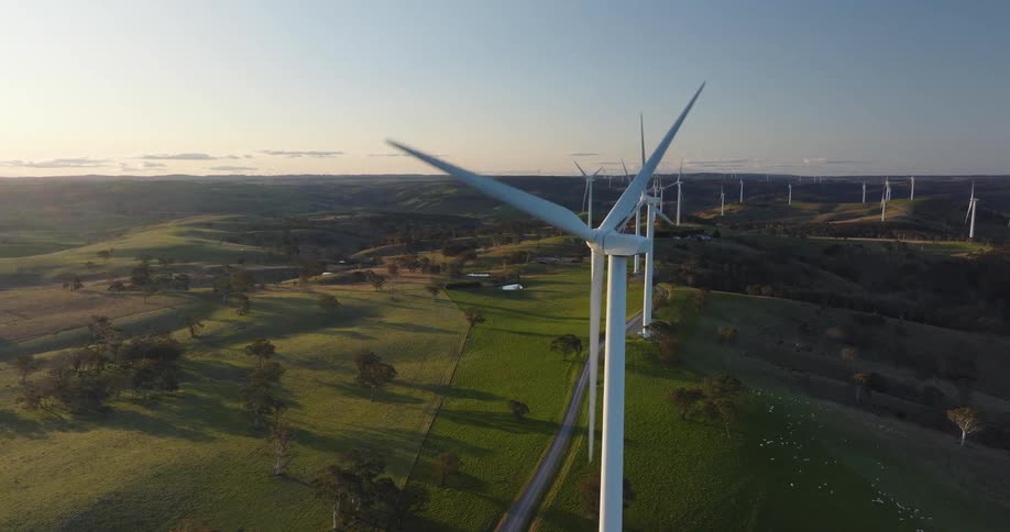 Wind turbines spin on a wind farm along a rural road