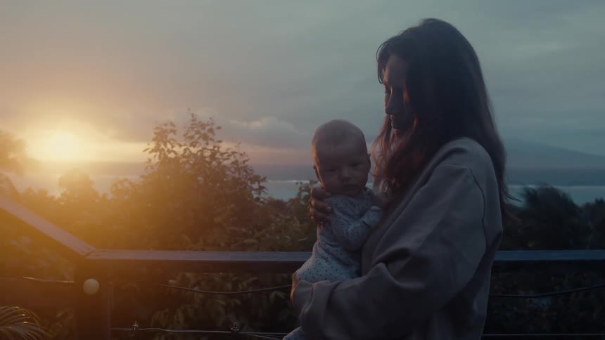 A mother holds her infant child outside and watches the sun rise