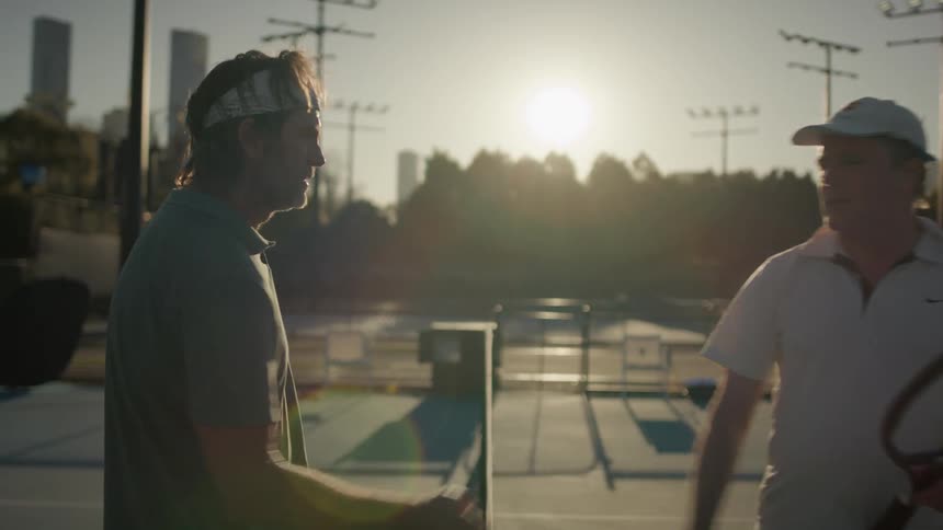 Two men greeting each other on the tennis court while holding their tennis rackets