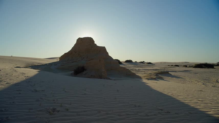 The sun shines behind sand dune in the desert