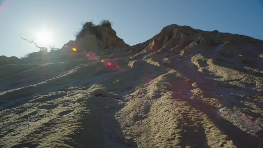 A gray mountain sits in front of a blue sky with the sun peeking out