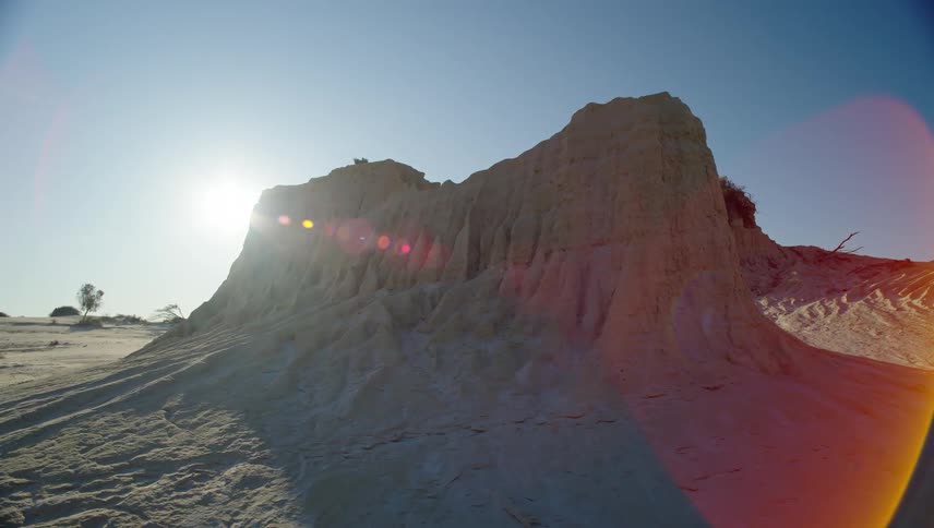 The sun shines behind sand dune against the blue sky in the desert