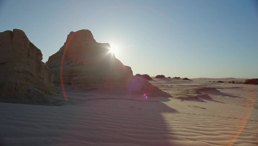 Sun shines behind a rock formation in the desert