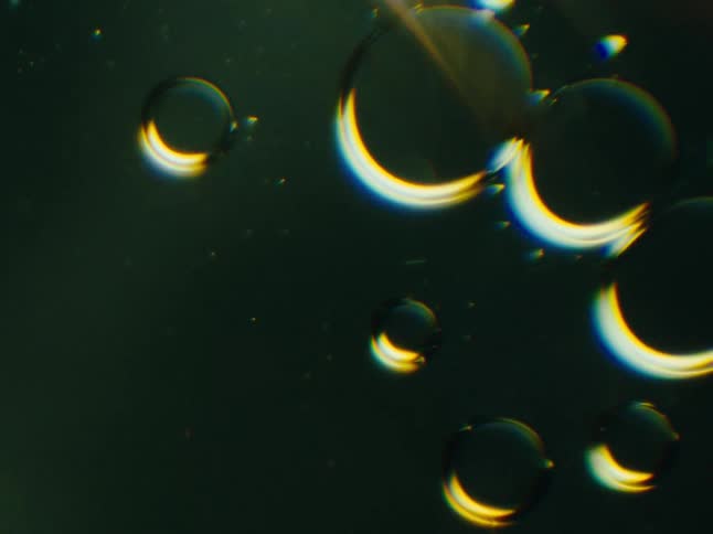 Yellow light shines on black orbs floating in the darkness as they fade away in a bright flare