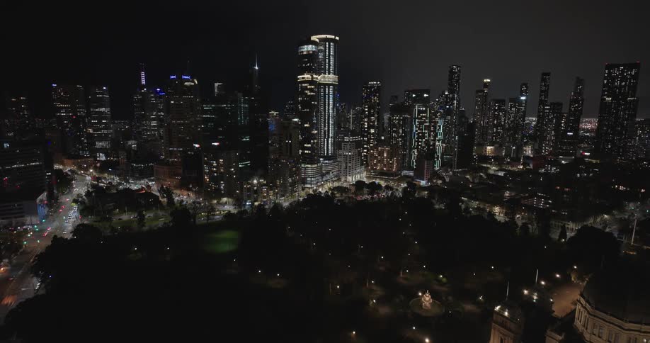 Lights on towers and buildings glow in the darkness as traffic moves across a bridge into downtown
