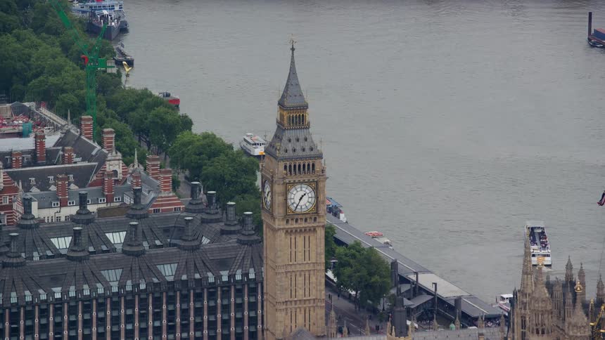 Big ben towers over nearby buildings near busy river