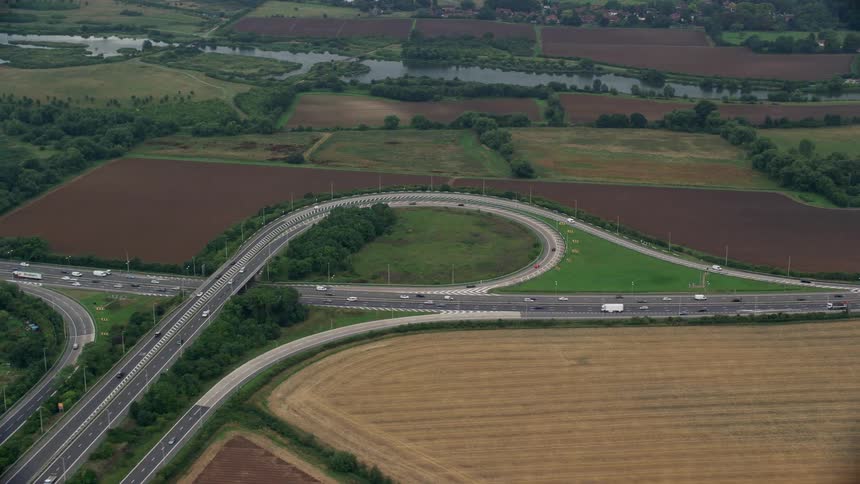 Aerial view of cars and trucks driving on highway near the fields and suburban area
