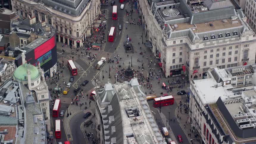 An aerial view of a busy city intersection with tall buildings cars red buses trucks pedestrians and cyclists