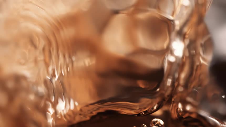 A clear brown liquid being poured into a glass container