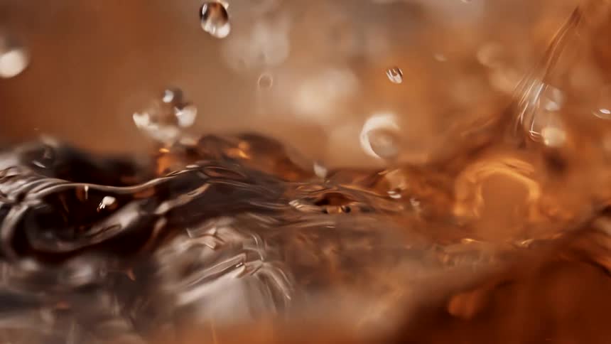 Droplets of a clear brown liquid falling into a glass container