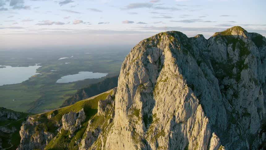 A cross stands on top of a rocky mountain overlooking a river under a cloudy sky