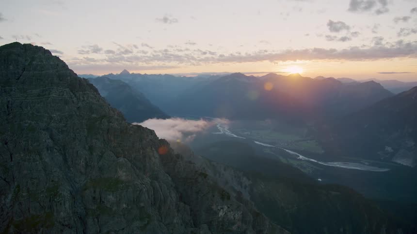 Aerial view of a landscape with a mountain range and the sunrise on the horizon