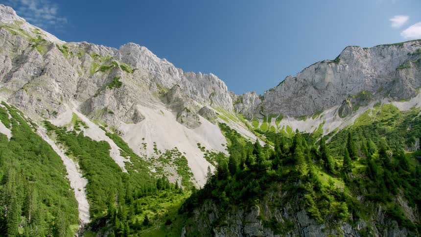 The sun shines upon forested mountains with mountains in the distance