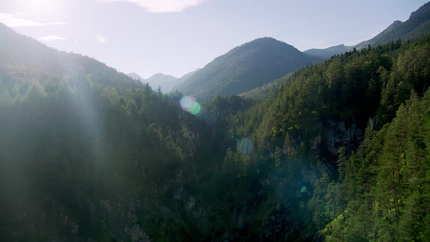 The sun shines upon heavily forested mountains with mountains in the distance