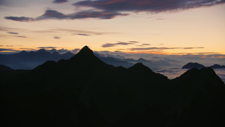 Fog fills valleys between mountains silhouetted against red tinted sky