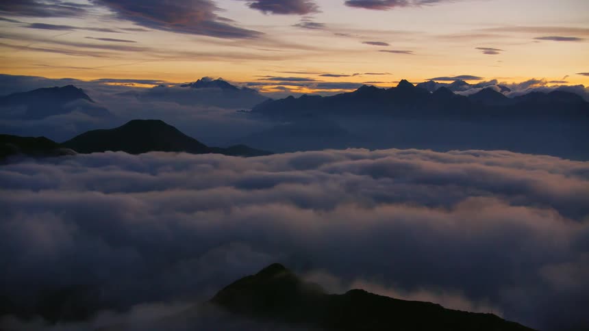 Tops of silhouetted mountains peak through low lying clouds under a red tinted sky