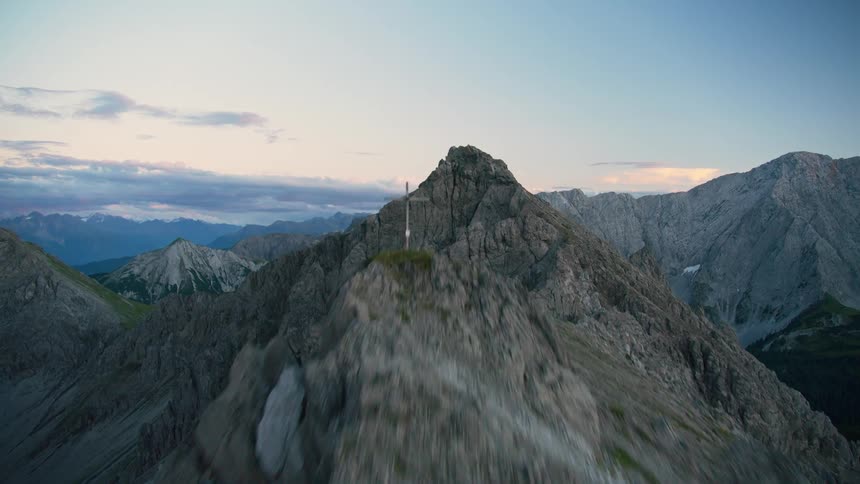Aerial of cross topped ridge overlooking green valley in mountainous terrain under a red tinted sky