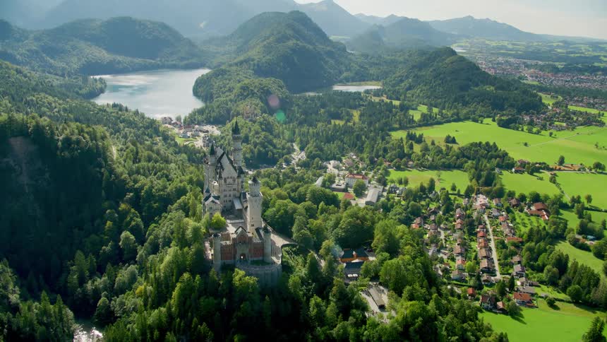 A castle at the edge of a cliff covered in green vegetation close to a town nearby in low land