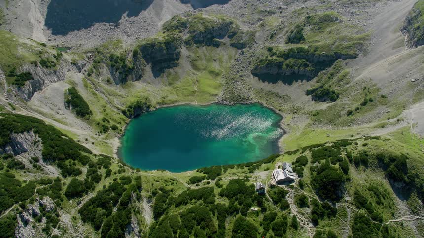 Paths cross mountain slope near buildings overlooking blue crater lake