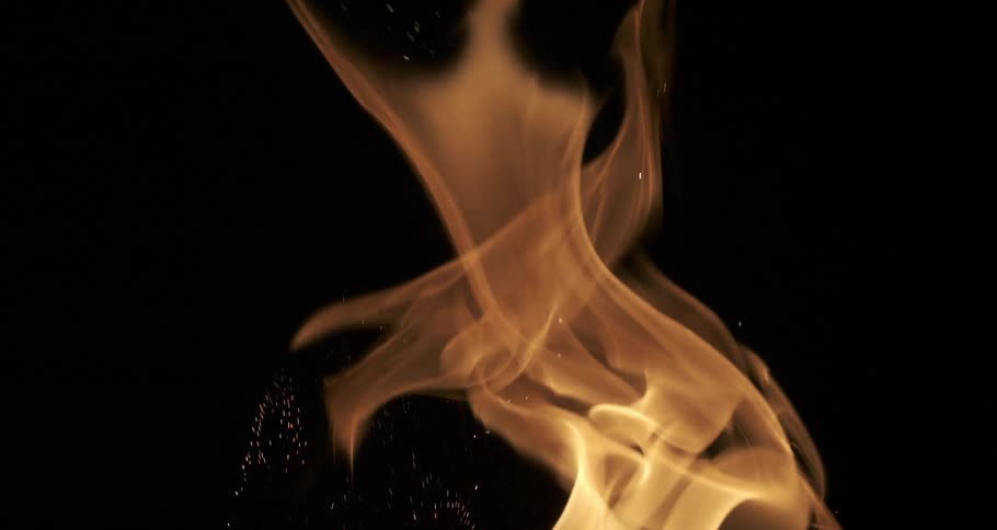 Glowing embers emerge from orange flames as they twist and rise in the darkness
