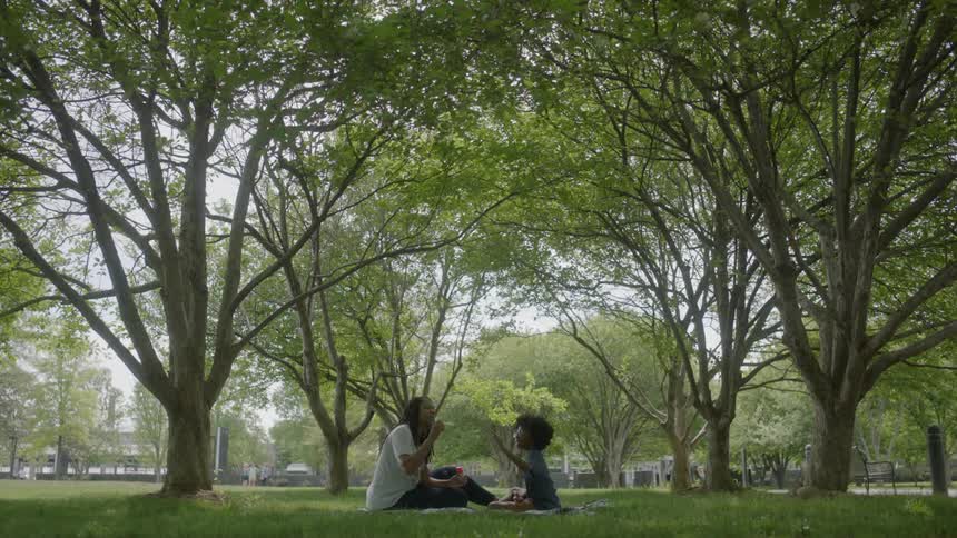 Two people sit in the grass together on a blanket blowing bubbles