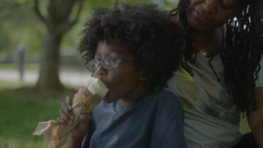 A boy eats ice cream as a woman watches