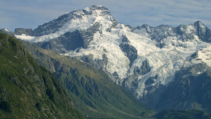 Multiple green mountains abut larger snow covered mountains and glaciers