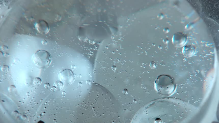 Air bubbles cluster pop float around merging and bumping against one another in a clear slightly bluetinged liquid