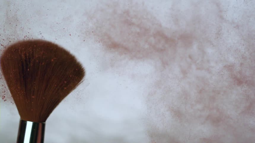 A makeup brush throwing red dust through its bristles to the right