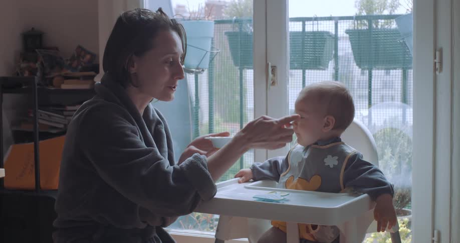 A hand feeding food into the mouth of her baby who is sitting