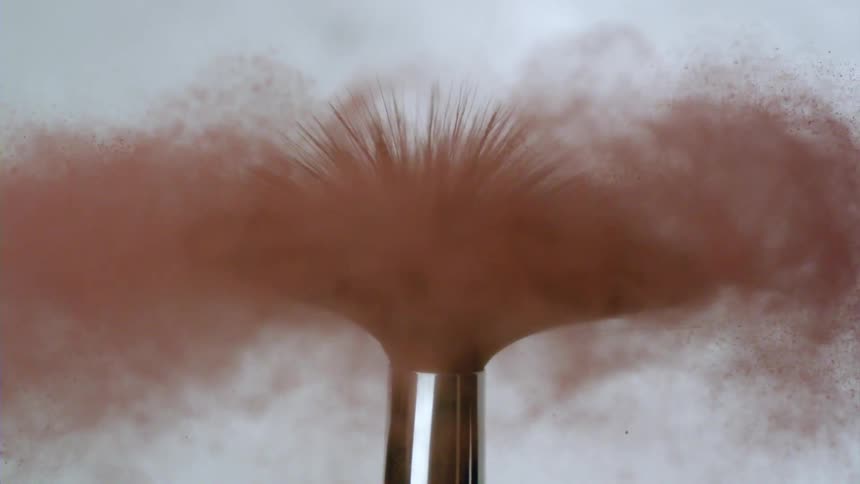A makeup brush with several bristles expelling red dust