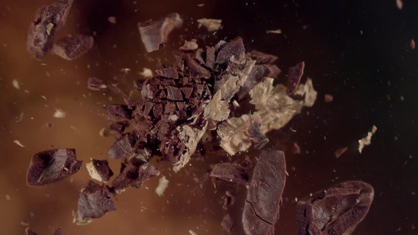 A closeup of a coffee bean as it explodes and pieces scatter in the air