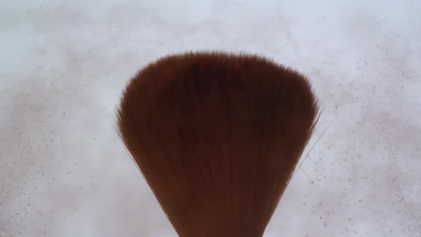 The bristles of a brush moving and throwing red dust everywhere