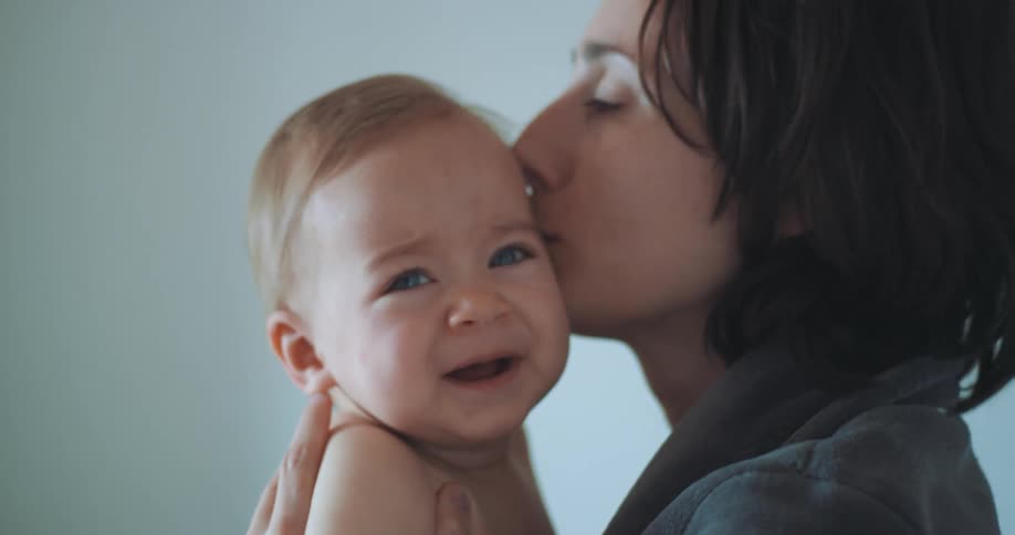 A mother kissing and caring for her baby who is on her lap and crying