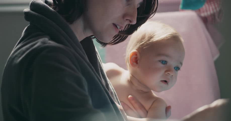 A mother holds her baby in one hand and looks at something in the other