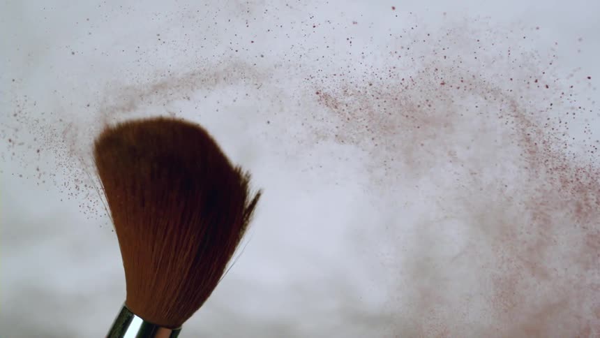 A large make up brush flings red powder off of it