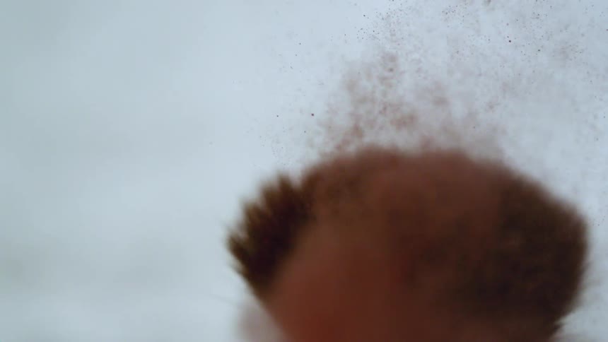 A makeup brush shakes as red powder flies into the air