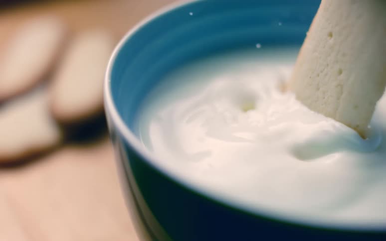 A cookie dipping on a cup of milk