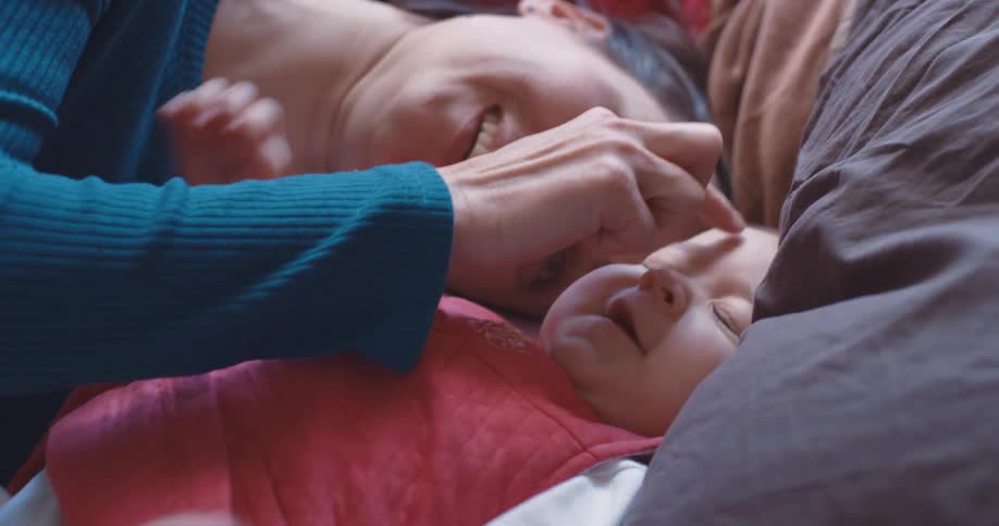 A mother is laying down and walking her fingers along her baby daughters chest