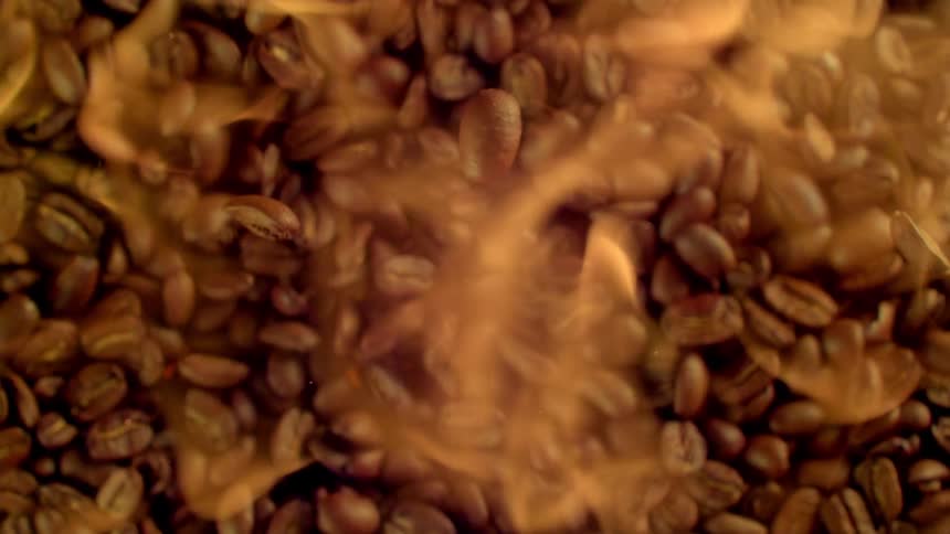 Several coffee beans falling in a pile as smoke comes out