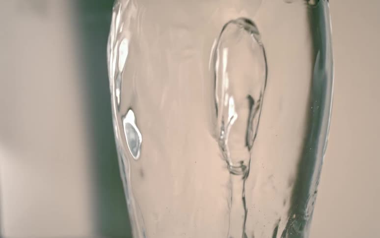 Clear water overflows in a clear glass in slow motion