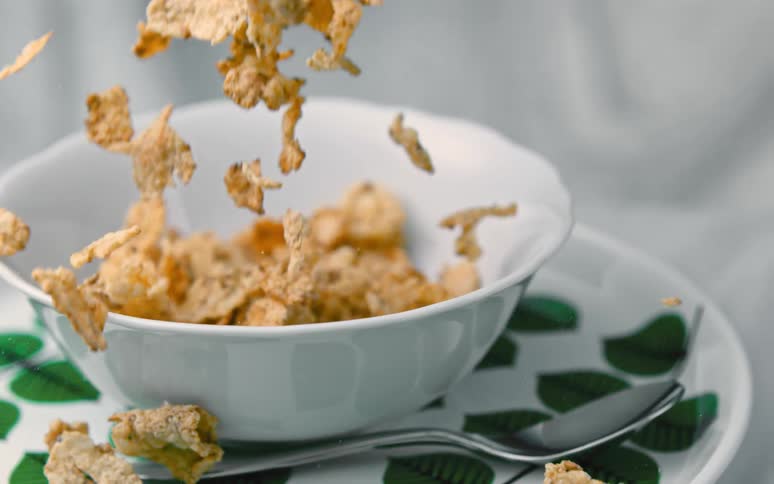 Corn flakes fall into a white ceramic bowl