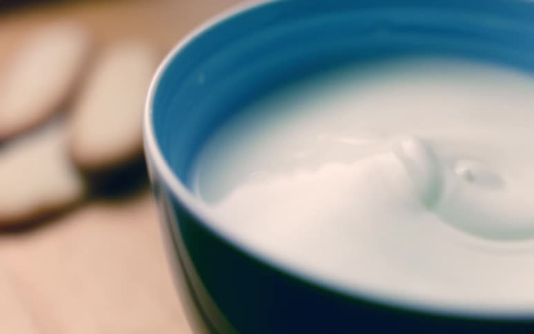 Falling drops create ripples in cup of milk on table near cookies