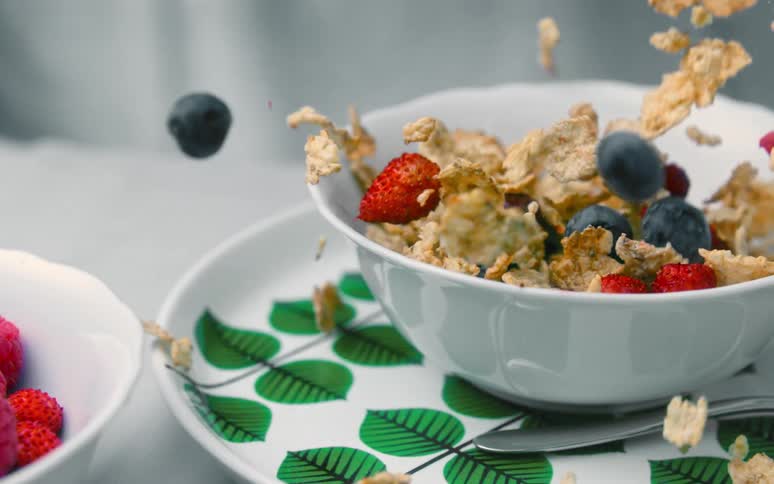 Cereal grains and strawberry and blueberry berries falling into a bowl