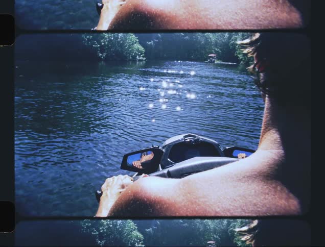 A man driving a watercraft in water surrounded by trees and being reflected by sunlight