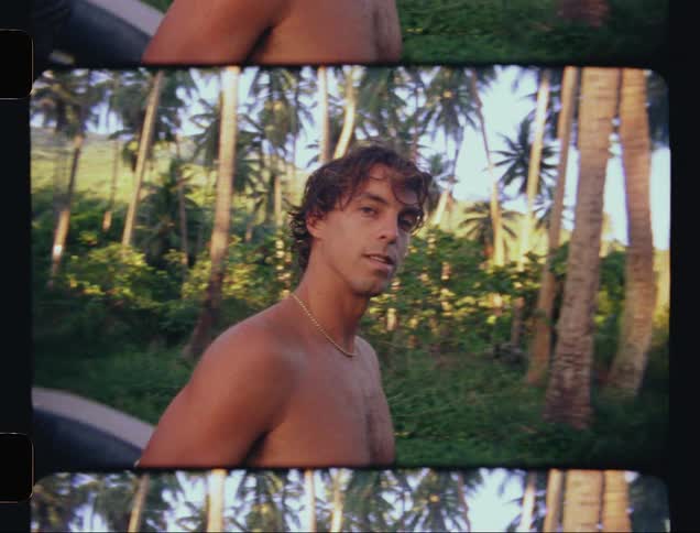 Closeup of a man with his surfboard walking in a tropical forest