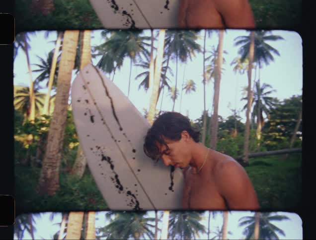 Portrait of a man with a surfboard walking in a tropical forest